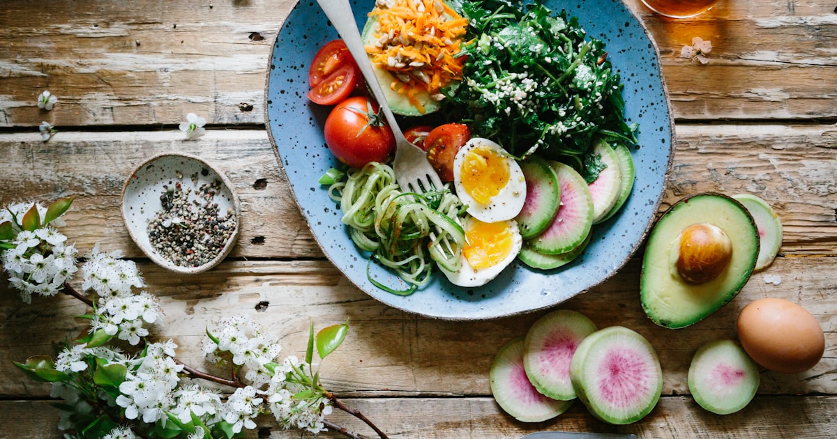 A colorful plate with grilled chicken, eggs, avocado, and vegetables